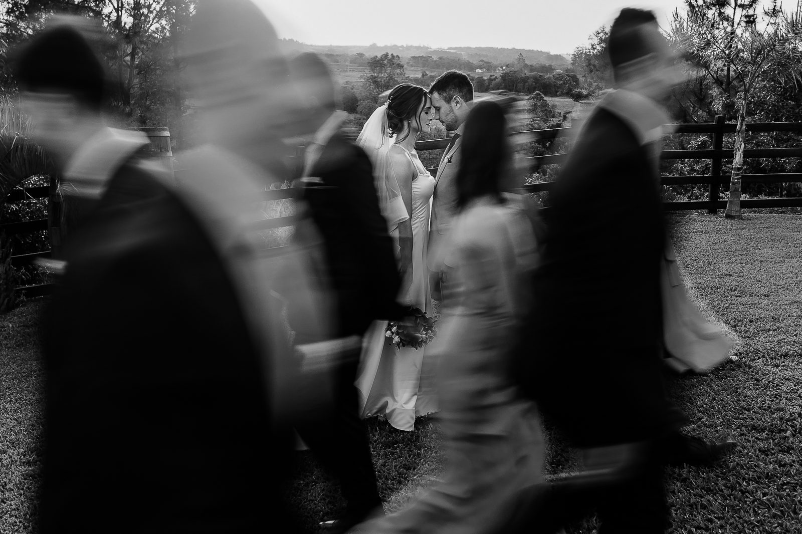 Bride and groom, still, as the wedding party moves